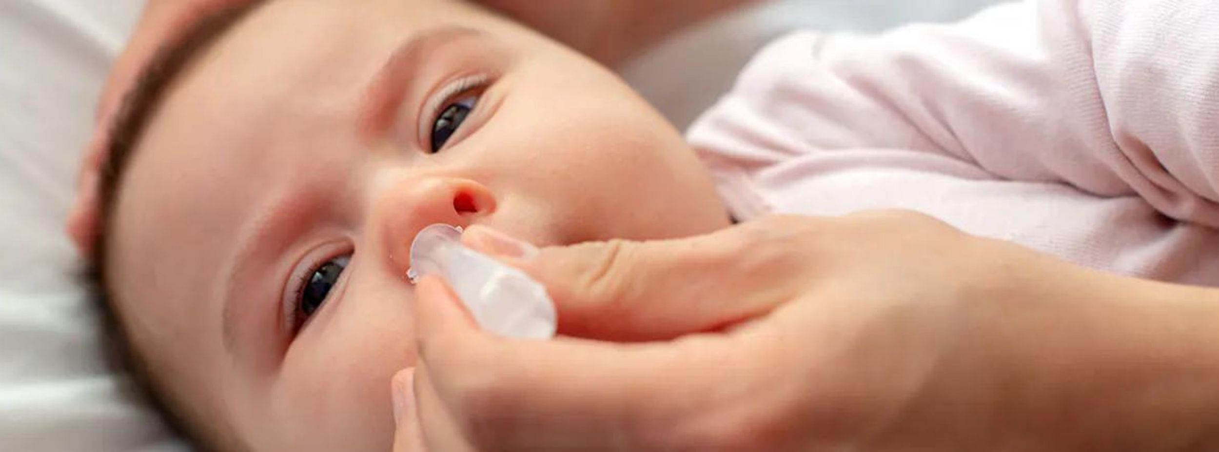 Bebis får näsdroppar med pipett av en vuxen hand medan den ligger ner på en säng.
