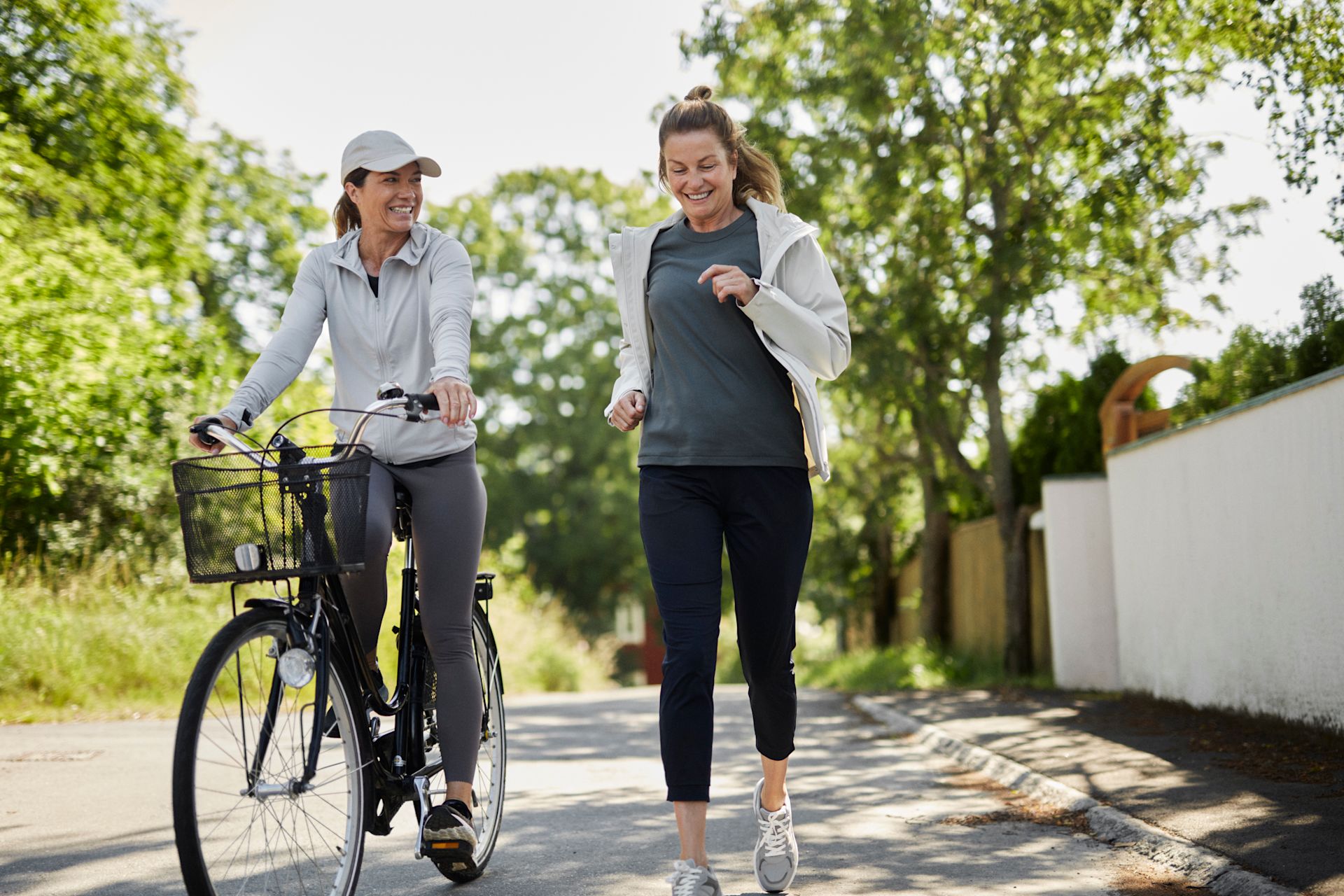 Två kvinnor är utomhus och motionerar, den ena springer och den andra cyklar. 
