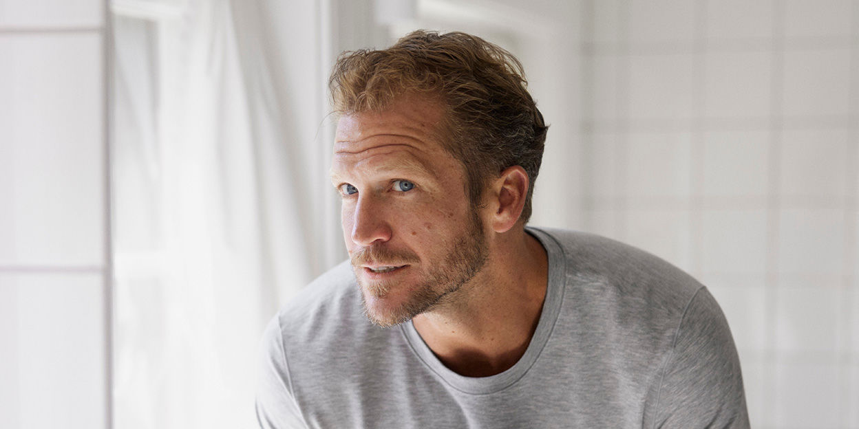 Man i badrumsmiljö står framför en spegel i lätt profil och speglar sig. 