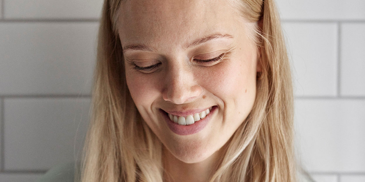 Kvinna som ler i badrum. Kollar snett nedåt. 