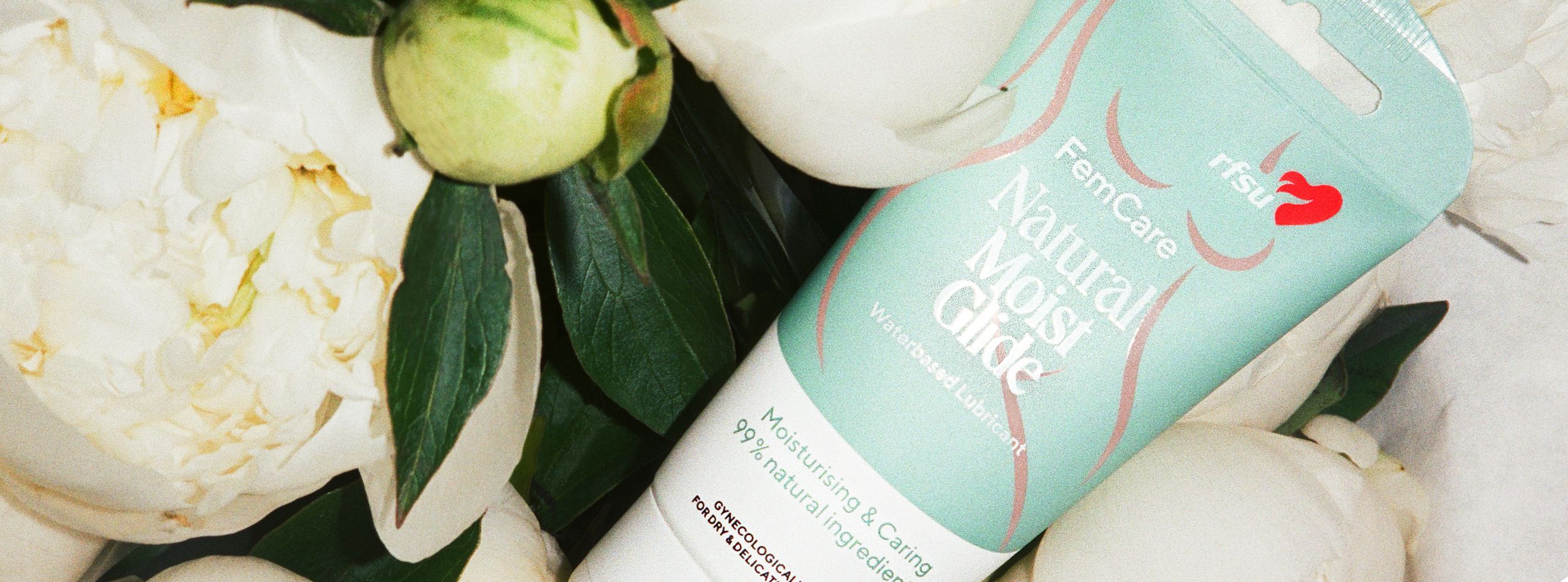 Tub med RFSU FemCare Natural Moist Glide vattenbaserat glidmedel ligger bland vita pioner.