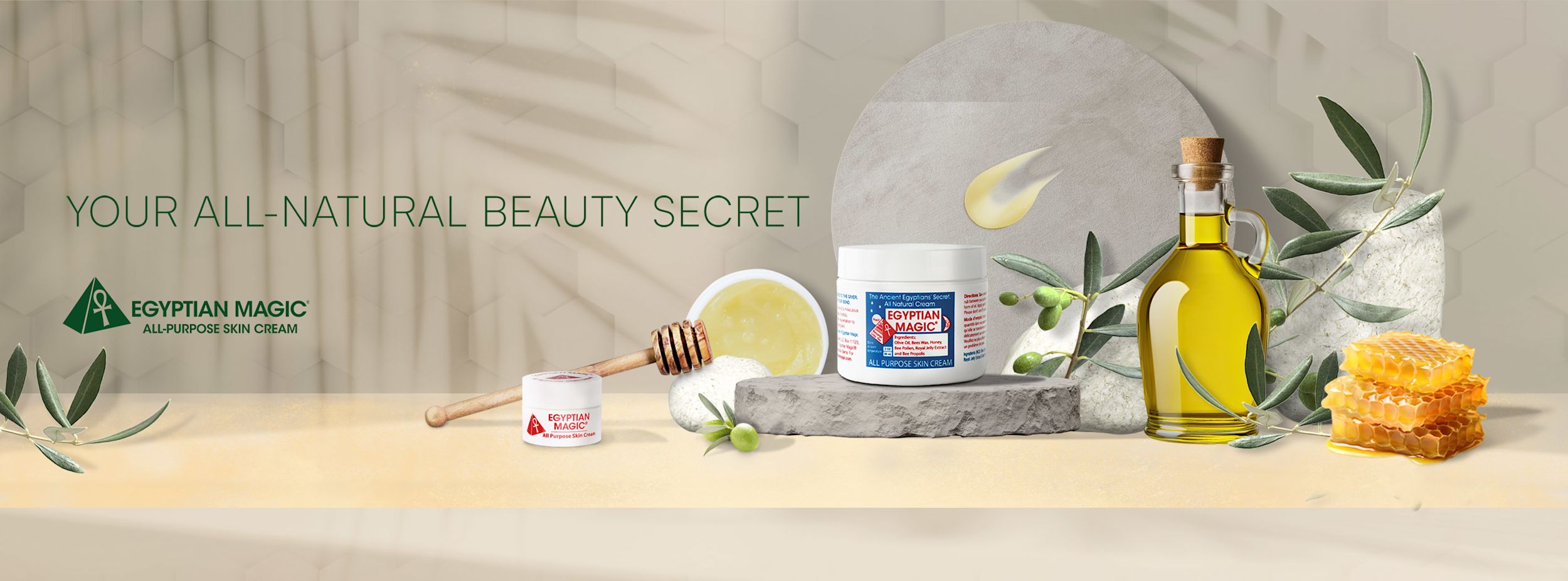 Burk med Egyptian Magic hudkräm står på ett bord med olivolja, bivax, honung, olivkvistar och texten "Your all-natural beauty secret".