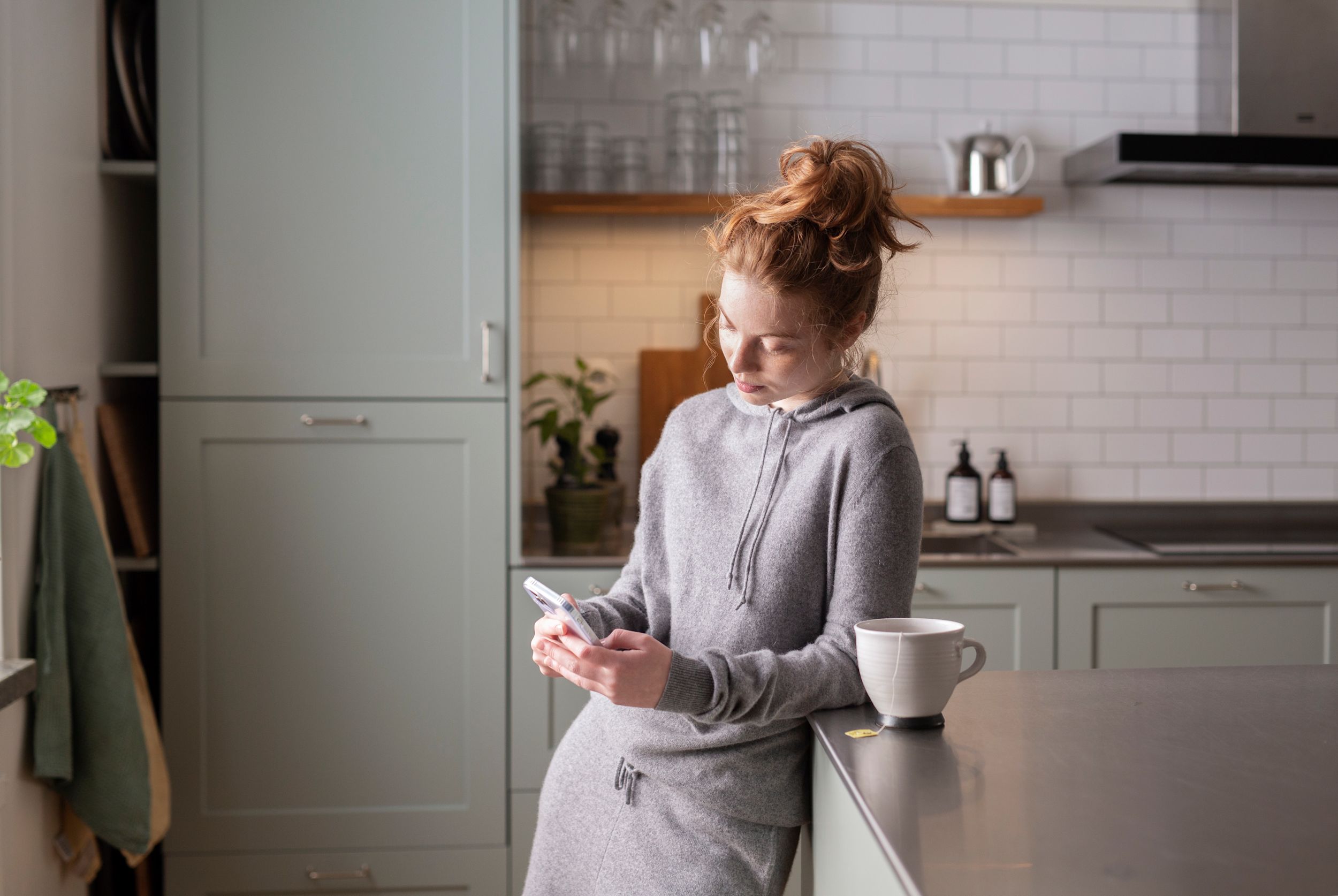 Tjej i tonåren står i köket och tittar på sin mobiltelefon.