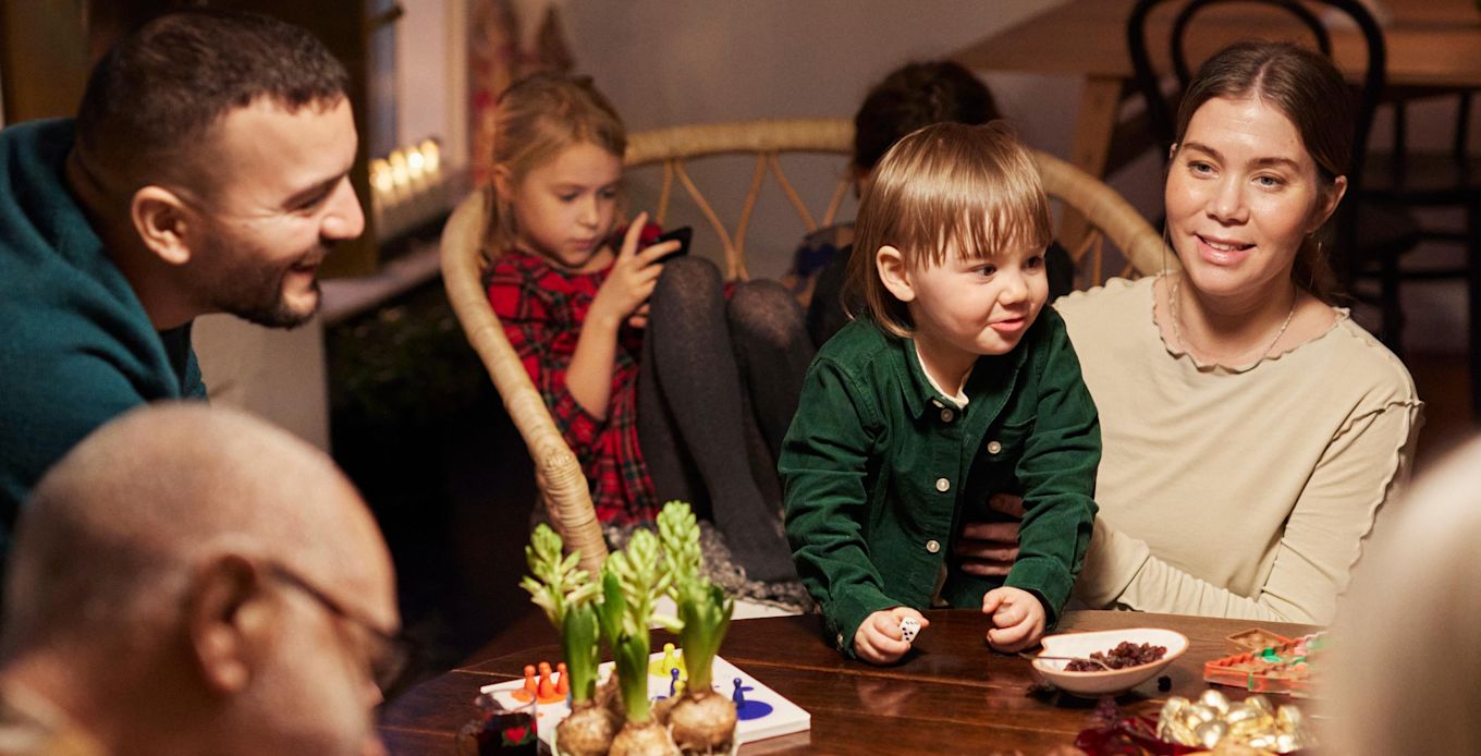 Familj och släkt sitter tillsammans och pratar och fikar runt ett bord på julen.