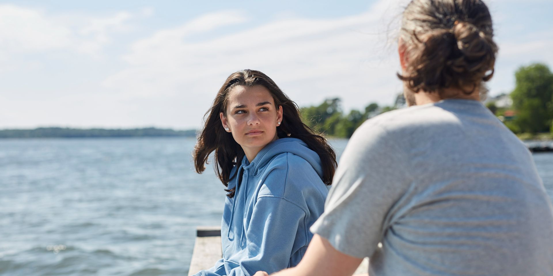 Pappa och tonårsdotter sitter på en brygga vid vattnet.