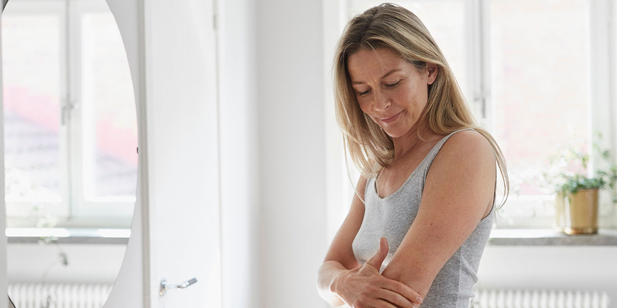 Kvinna i ljus inomhusmiljö håller på att avsluta sin insmörjning av armen. 