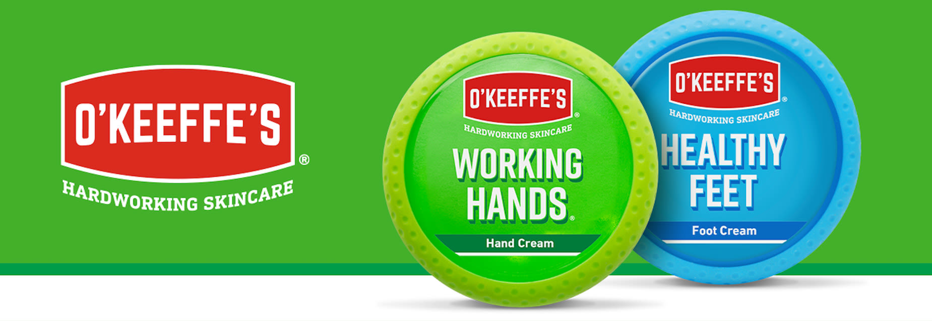 Två burkar O’Keeffe’s hudvård: Working Hands handkräm i grönt och Healthy Feet fotkräm i blått, mot grön bakgrund.