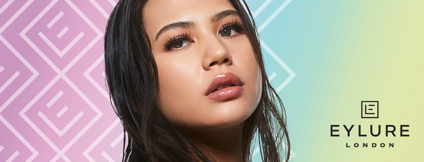 Kvinna med långa, fylliga ögonfransar och glansiga läppar poserar mot pastellfärgad bakgrund, logotypen Eylure London syns till höger.