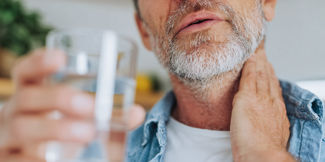 Man som håller i ett glas vatten och håller sig för halsen. 