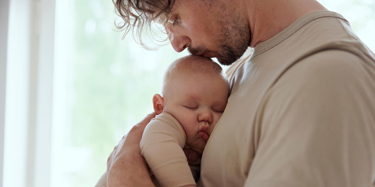 En man håller en liten bebis och kysser den på huvuvdet.