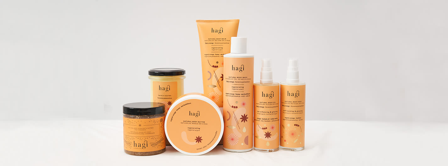Sju Hagi hudvårdsprodukter med orange etiketter står uppradade på vit bakgrund, inklusive kroppssmör, duschgel och kroppsmist.