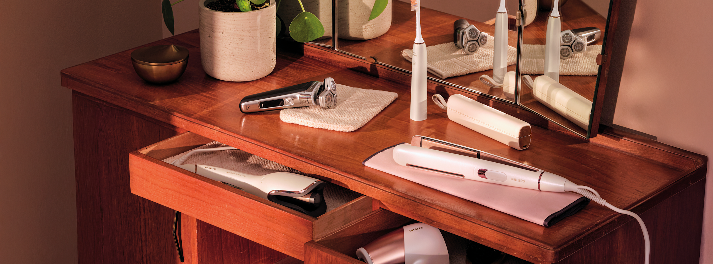 Elektriska skönhetsprodukter från Philips, inklusive rakapparat, eltandborste och hårstyler, placerade på ett trätoalettbord med spegel.