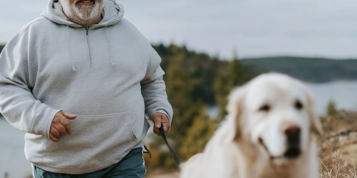Man i grå hoodie springer ute i naturen tillsammans med sin hund. Bilden är delvis skapad med AI.