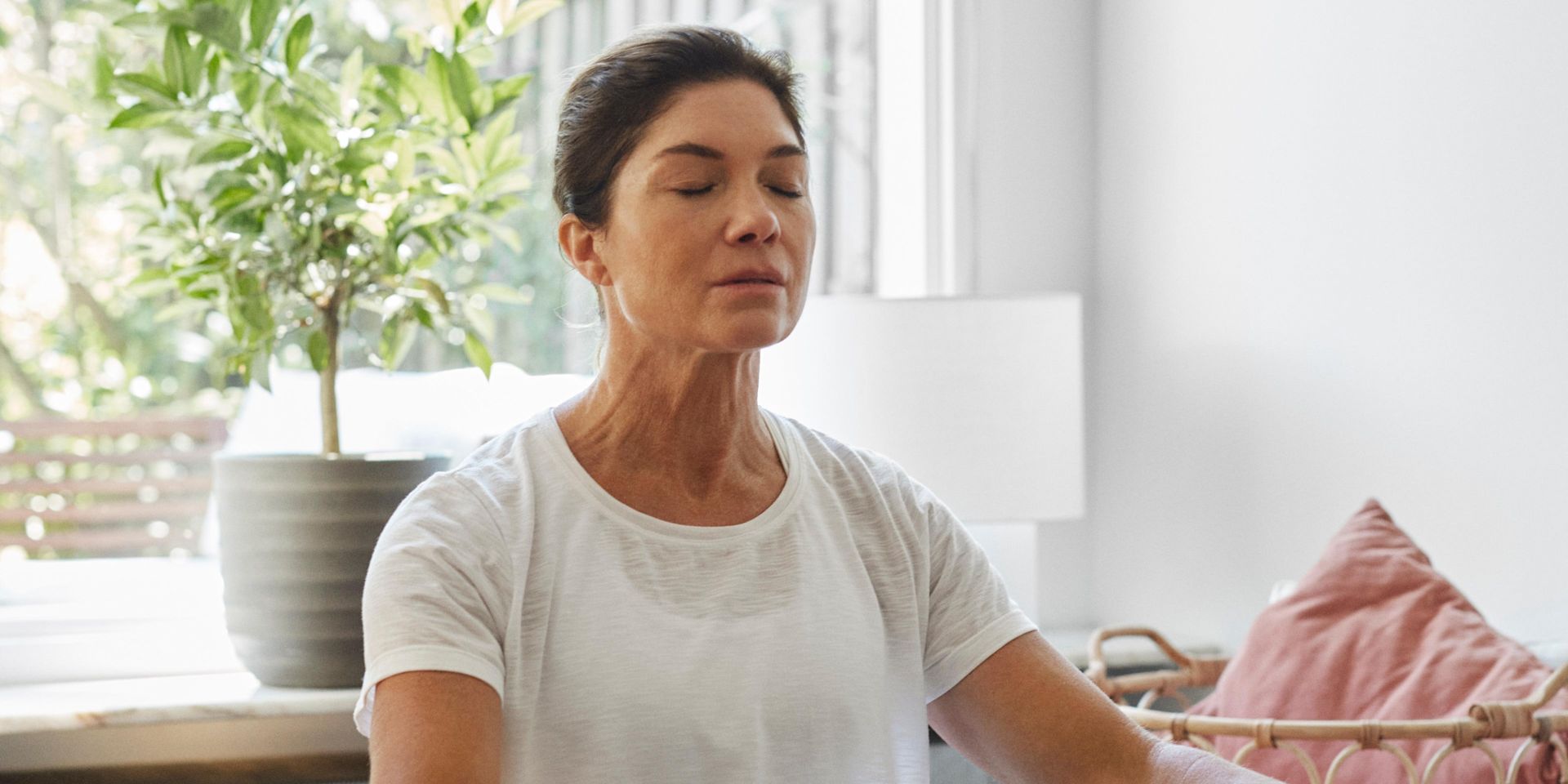 En kvinna sitter i yogaställning på golvet och blundar och andas djupt.